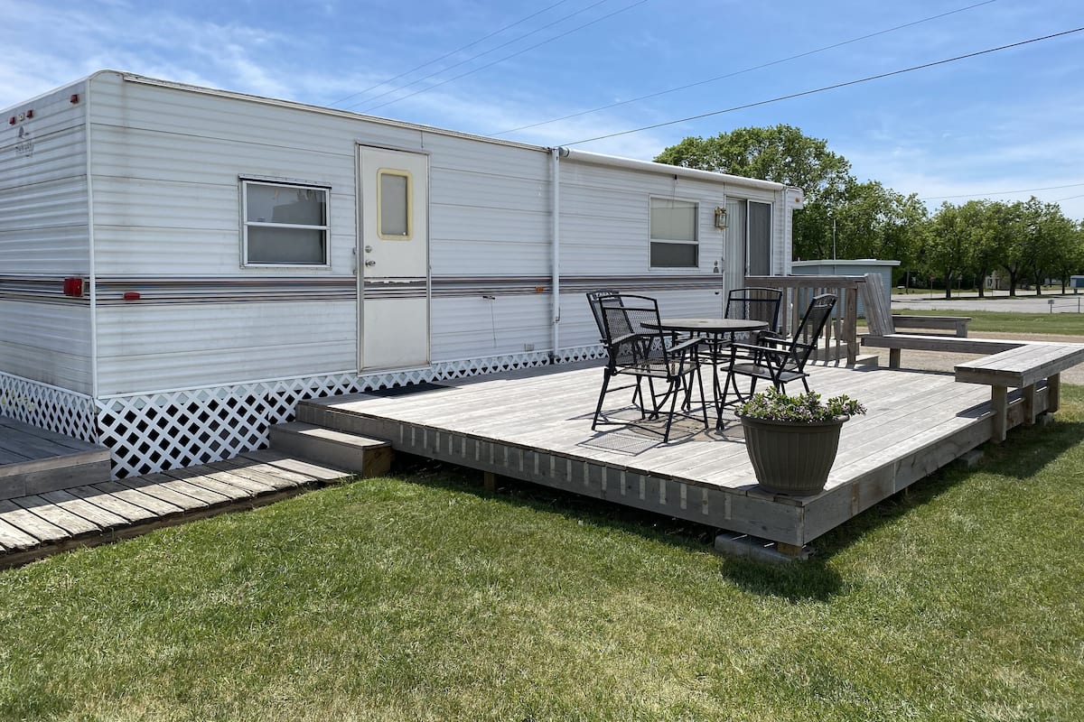 A mobile home with a patio area featuring a table and chairs, a small shed, and a fenced deck.
