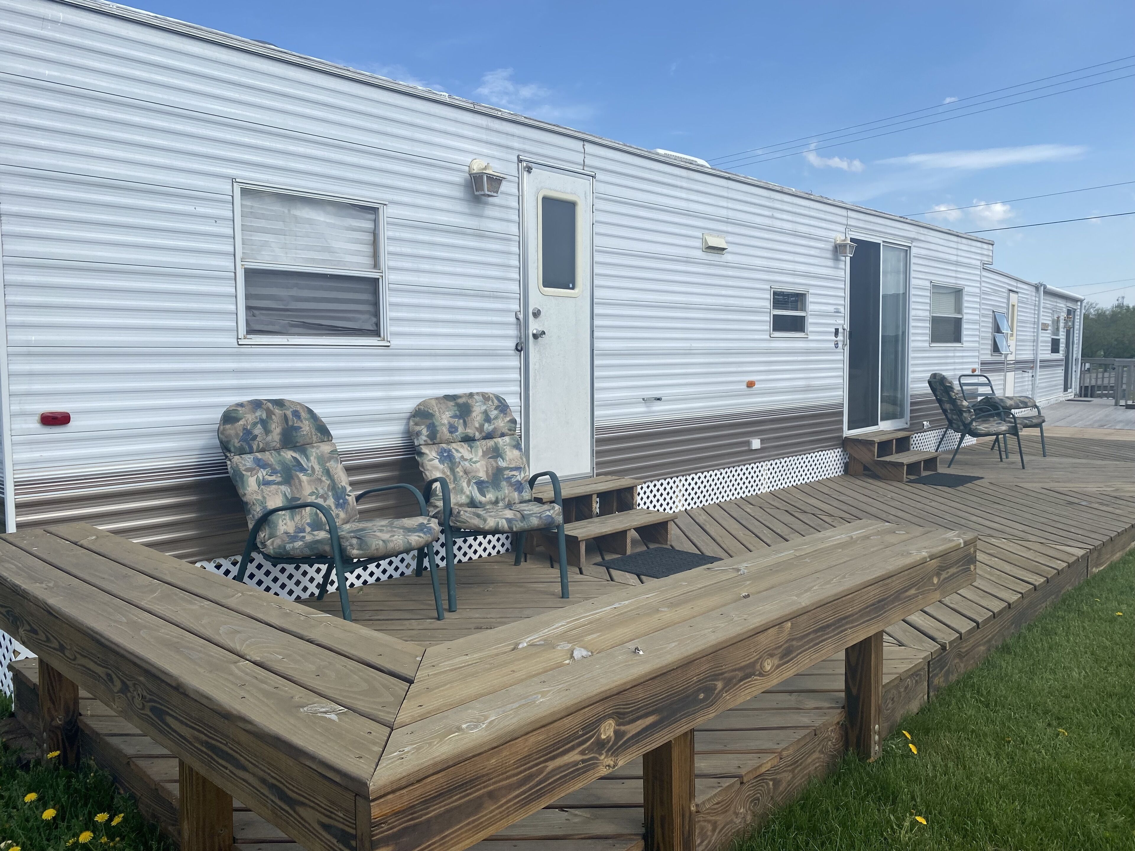 A mobile home with a deck, two chairs, and a small table.