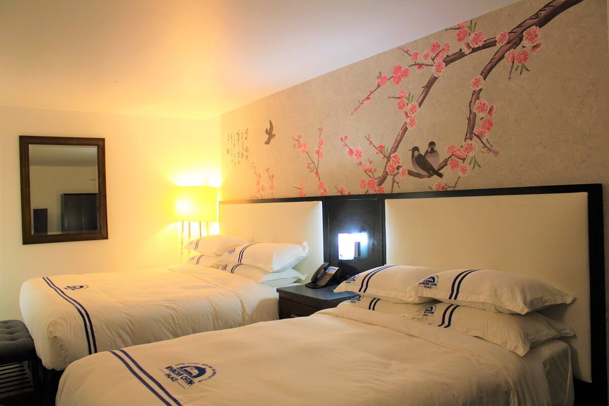 Habitación de hotel con dos camas, una mesita de noche con teléfono y una pared decorada con un mural floral.