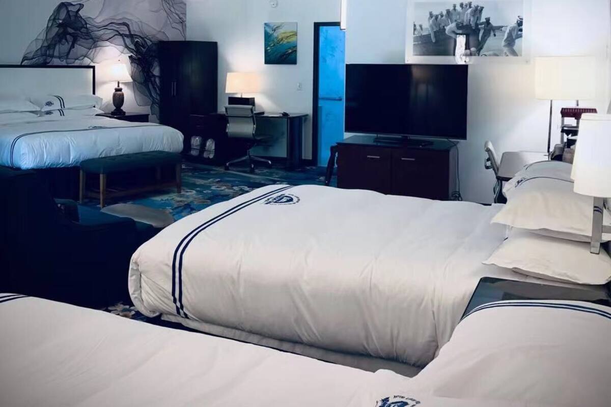 Habitación de hotel con dos camas, un escritorio, una silla, un televisor y obras de arte en las paredes.