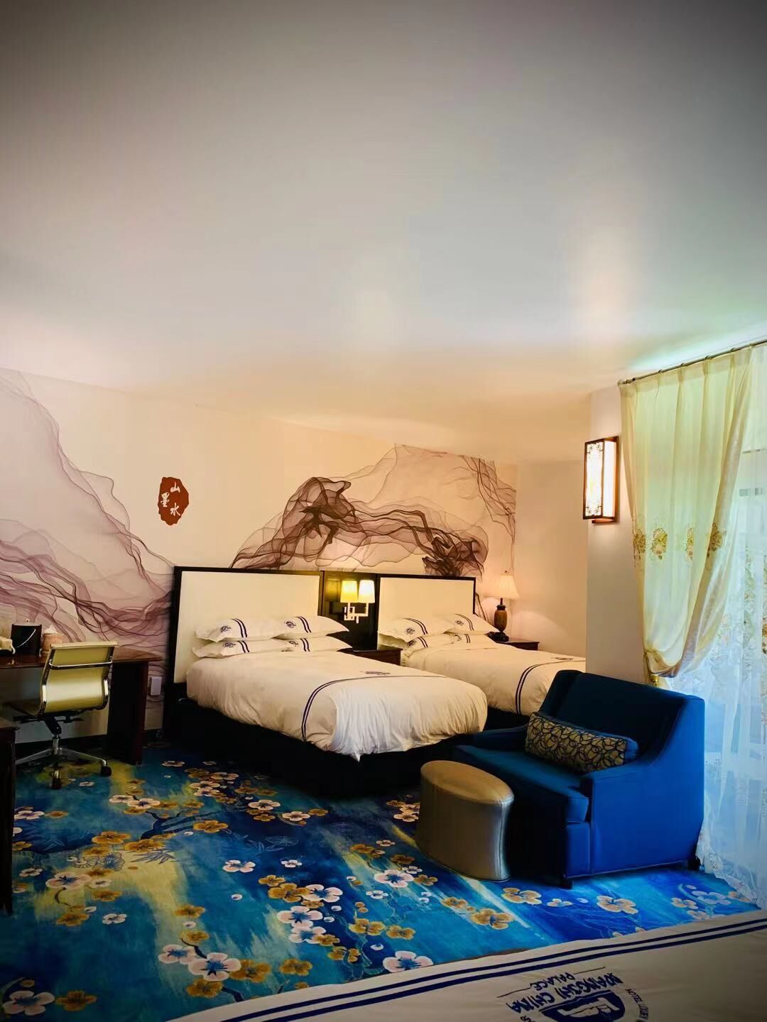 A hotel room with two beds, a desk, a chair, and a sofa.