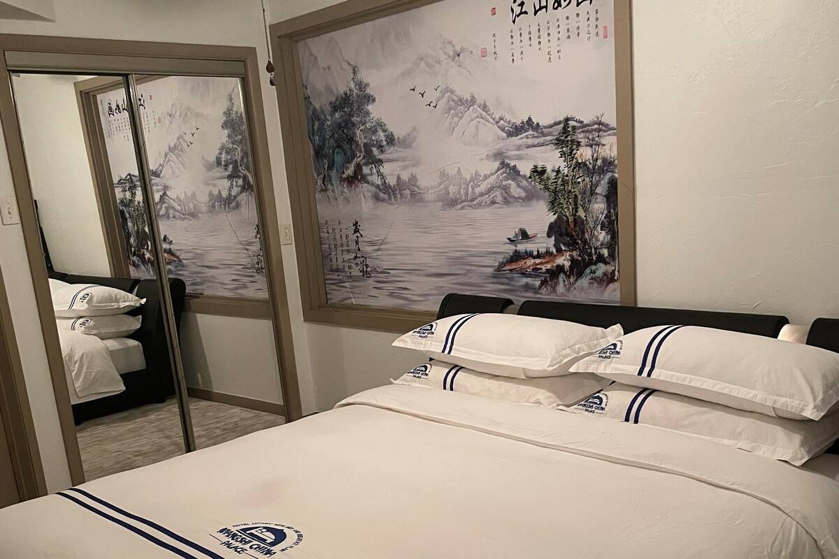 Habitación de hotel con cama, ventilador de techo, una pared con un cuadro y un espejo.