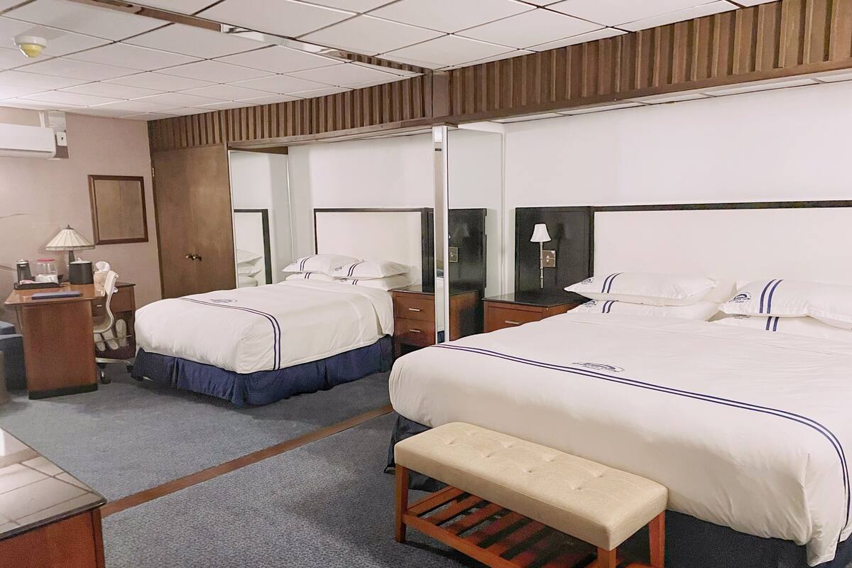 Habitación de hotel con dos camas, un escritorio, una silla, un banco, un espejo y un armario.
