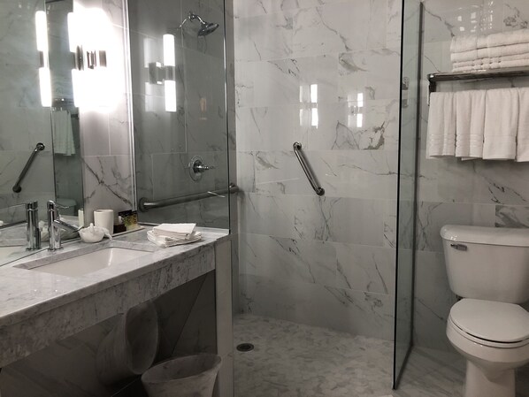 Une salle de bain moderne avec une douche à parois de verre, un sol carrelé en marbre, des toilettes blanches et un lavabo avec un miroir.