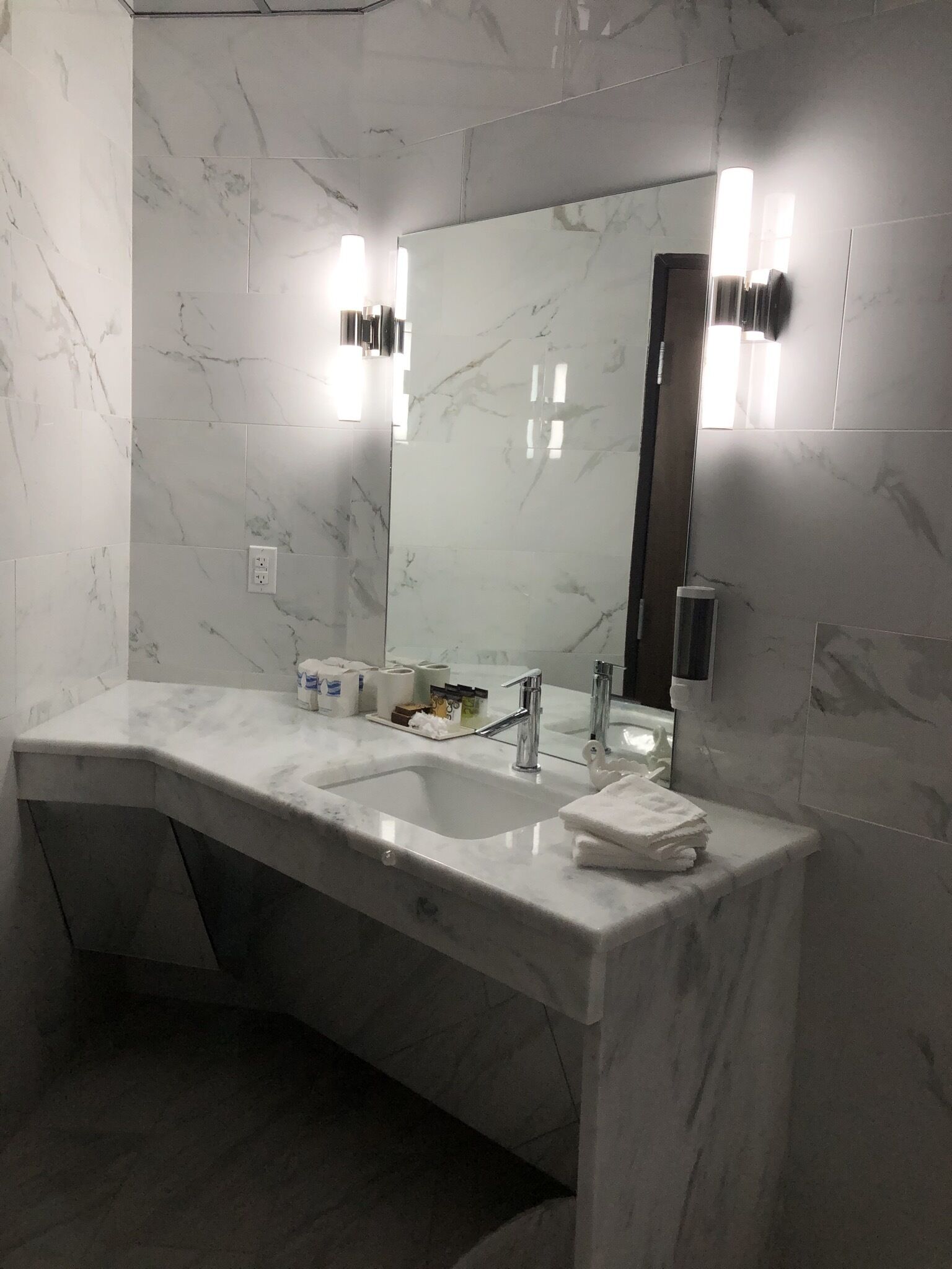 A modern bathroom with a marble vanity, two sinks, a large mirror, and wall-mounted lighting.