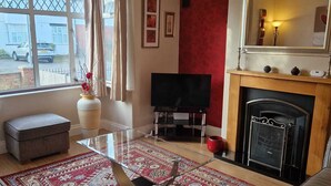 Una sala de estar con televisor, chimenea y un amplio ventanal con cortinas.