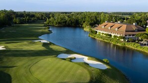 Un campo da golf con bunker e specchi d'acqua, circondato da alberi e un grande edificio con tetto rosso.