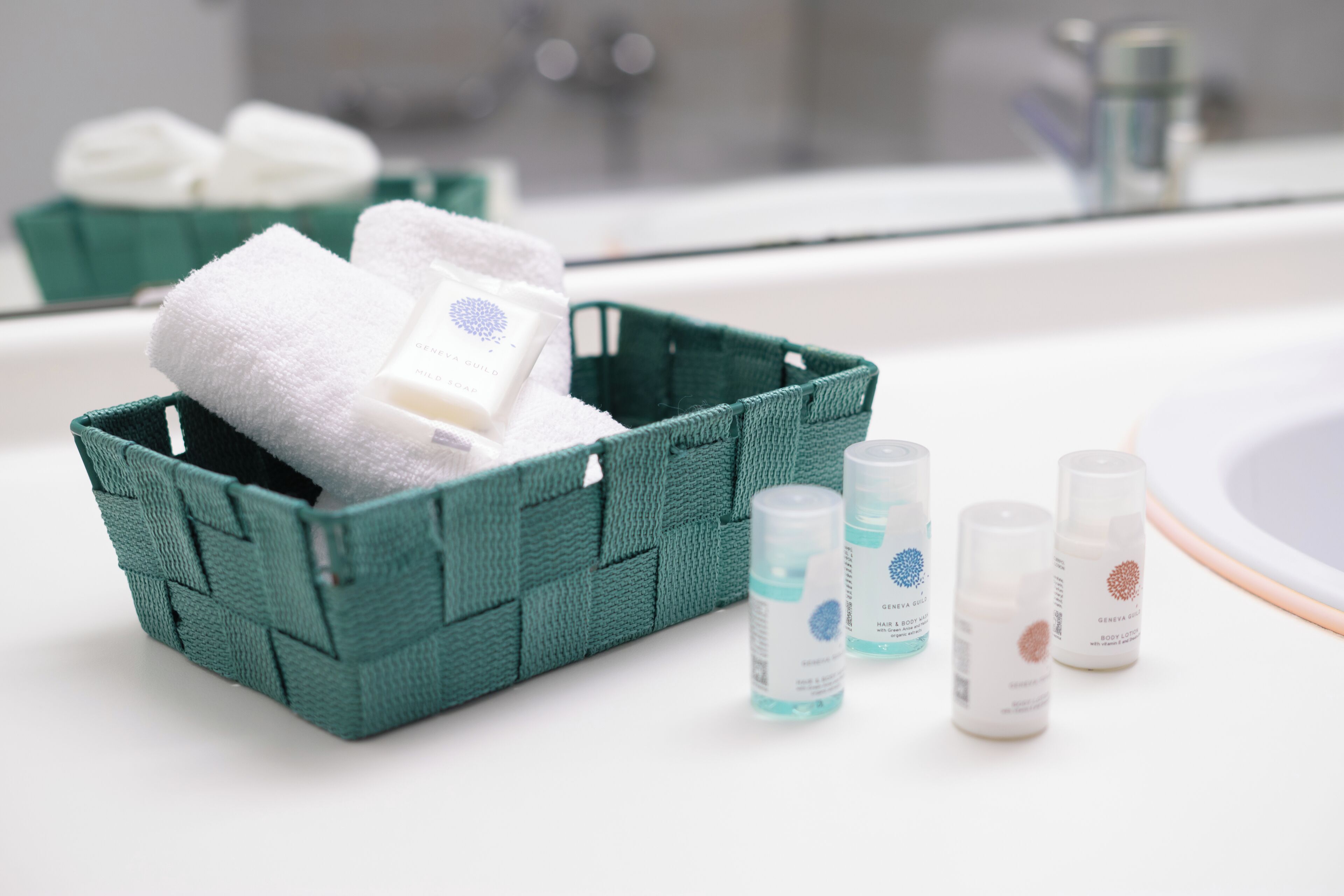 A bathroom with a green basket containing a white towel and a bottle of mild soap.