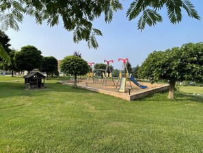 Enjoy a serene outdoor space with a playground featuring a slide and swings surrounded by lush greenery.