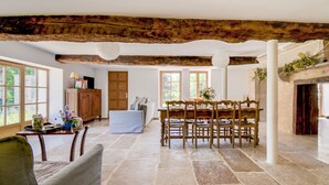 Una habitación amplia con suelo de piedra, muebles de madera y grandes ventanales.