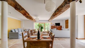 Comedor con una mesa de madera dispuesta para cuatro, rodeada de sillas, con vistas a una sala de estar y una ventana al fondo.