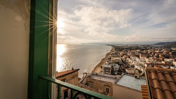 A coastal cityscape with buildings, a beach, and a view through a window with a green frame.
