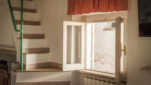 A staircase with a green handrail, a window with a red checkered valance, and a white door.