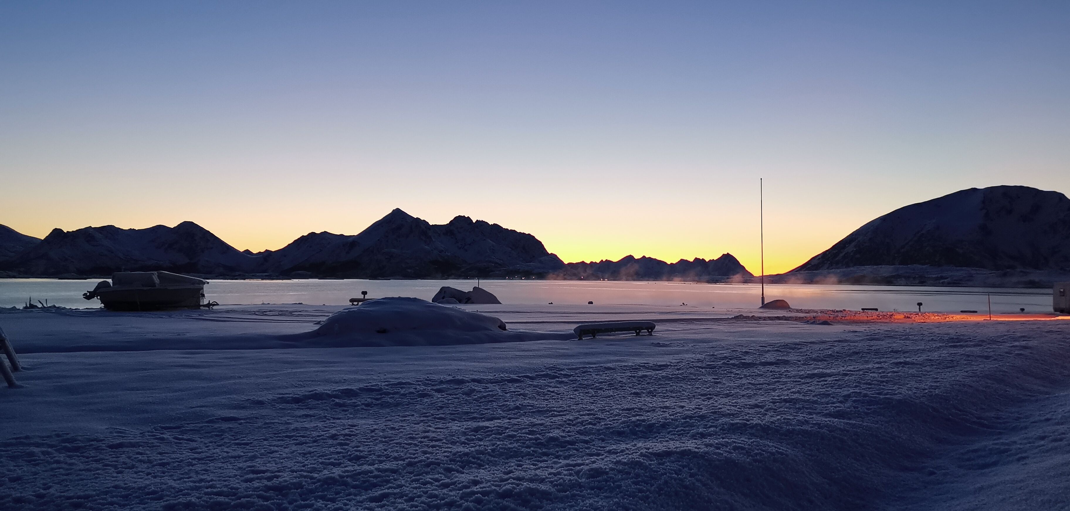 Ett snötäckt landskap med berg i bakgrunden och en frusen sjö eller flod i förgrunden.