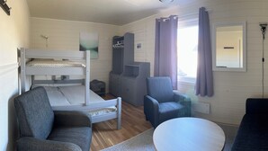 A room with a bunk bed, a chair, a sofa, a small table, and a window with curtains. - Oppmyre Camping (Oksnes)