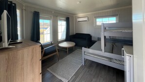 A compact room with a bunk bed, a small sofa, a desk with a chair, and a window with curtains. - Oppmyre Camping (Oksnes)