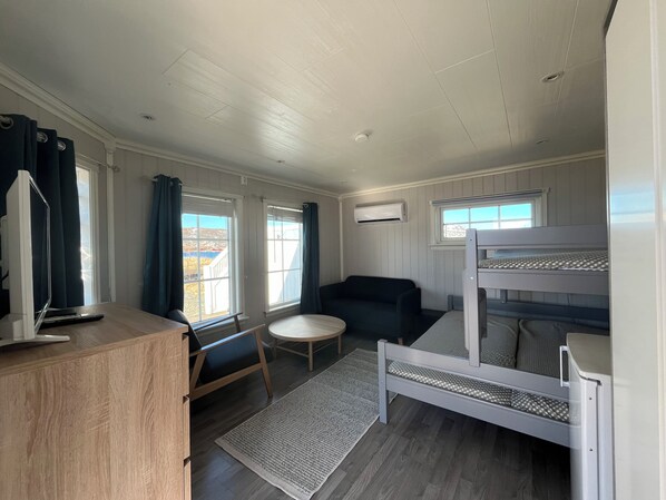Una habitación compacta con una cama litera, un pequeño sofá, un escritorio con silla y una ventana con cortinas.