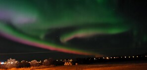 A night scene with a green aurora display over a rural landscape with distant lights. - Oppmyre Camping (Oksnes)