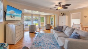 A spacious living room with a large gray sofa, a wooden coffee table, and a television displaying a beach scene. - River house with 2 boat docks (Astor)