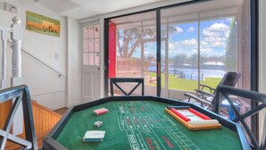 A craps table with dice and chips, a door leading outside, and a view of a lake. - River house with 2 boat docks (Astor)