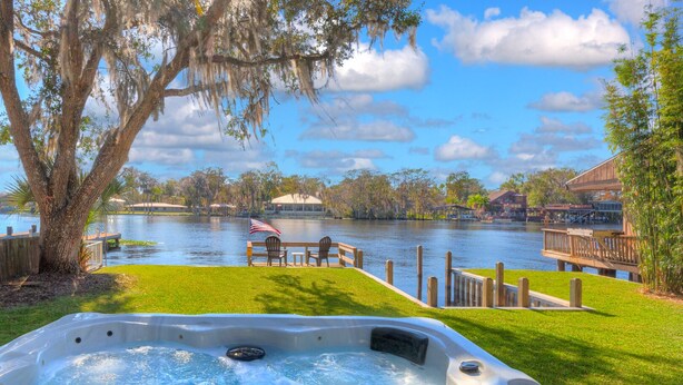 A hot tub with a view of a lake, wooden deck, and a gazebo in the background. - River house with 2 boat docks (Astor)