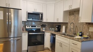 A modern kitchen with stainless steel appliances, white cabinetry, a granite countertop, and a black rug. - River house with 2 boat docks (Astor)