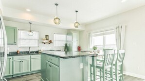 A modern kitchen with green cabinets, a central island, bar stools, pendant lighting, and a window with curtains. - 100K remodel Jan 2024 - Waterfront Bay/Beach House w/ boat parking private canal (Freeport)