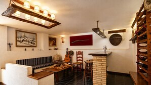 Une pièce chaleureuse avec un banc en bois, une guitare, un meuble à bouteilles et un mur rouge.