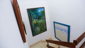 Un escalier avec une rampe en bois, un tableau représentant une scène de forêt et un tableau encadré accroché au mur.