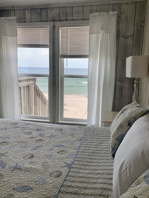 A bedroom with a large bed, a view of the beach, and a wooden wall.