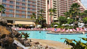 Et hotel med en stor swimmingpool, flere balkoner og palmer.