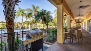 Eine Terrasse mit Grill, Sitzgelegenheit im Freien und Blick auf Palmen und einen Pool.