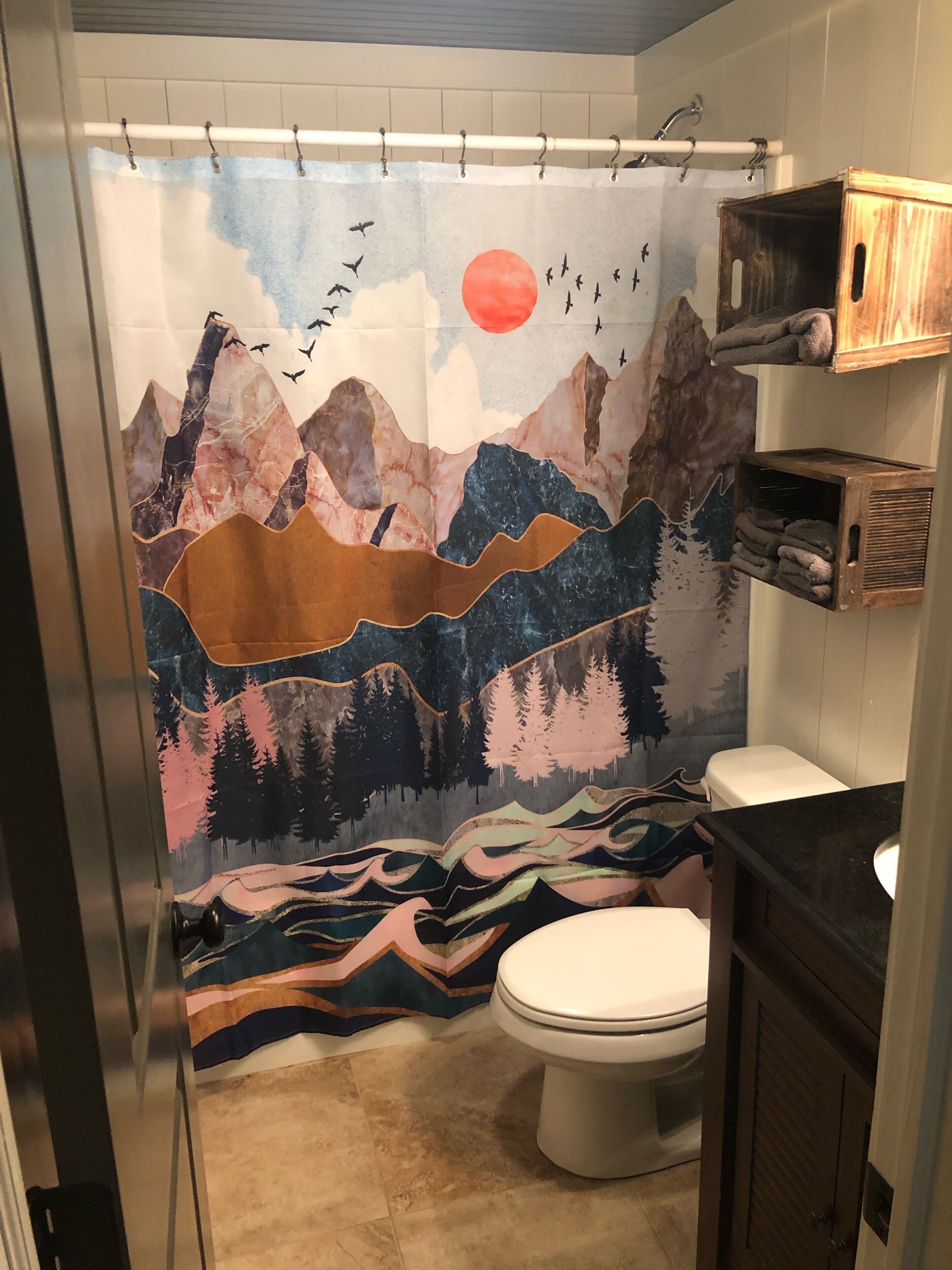 Ein Badezimmer mit Duschvorhang mit Berglandschaft, Toilette und Holzregalen mit Handtüchern.