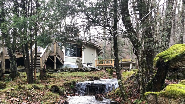 Una cabana rústica amb terrassa de fusta i una petita cascada.