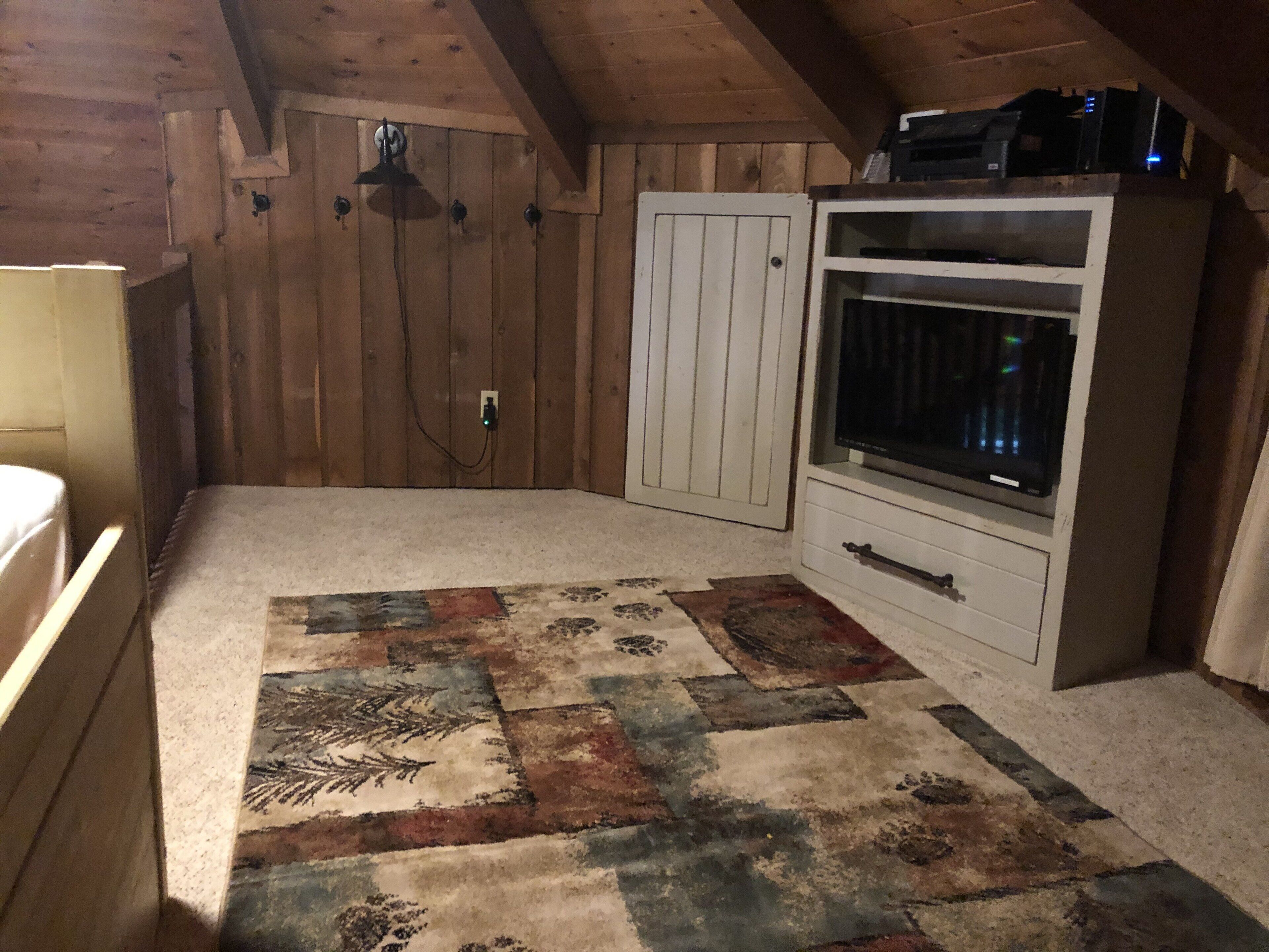 A room with a wooden ceiling, a white cabinet with a television, and a patterned rug.
