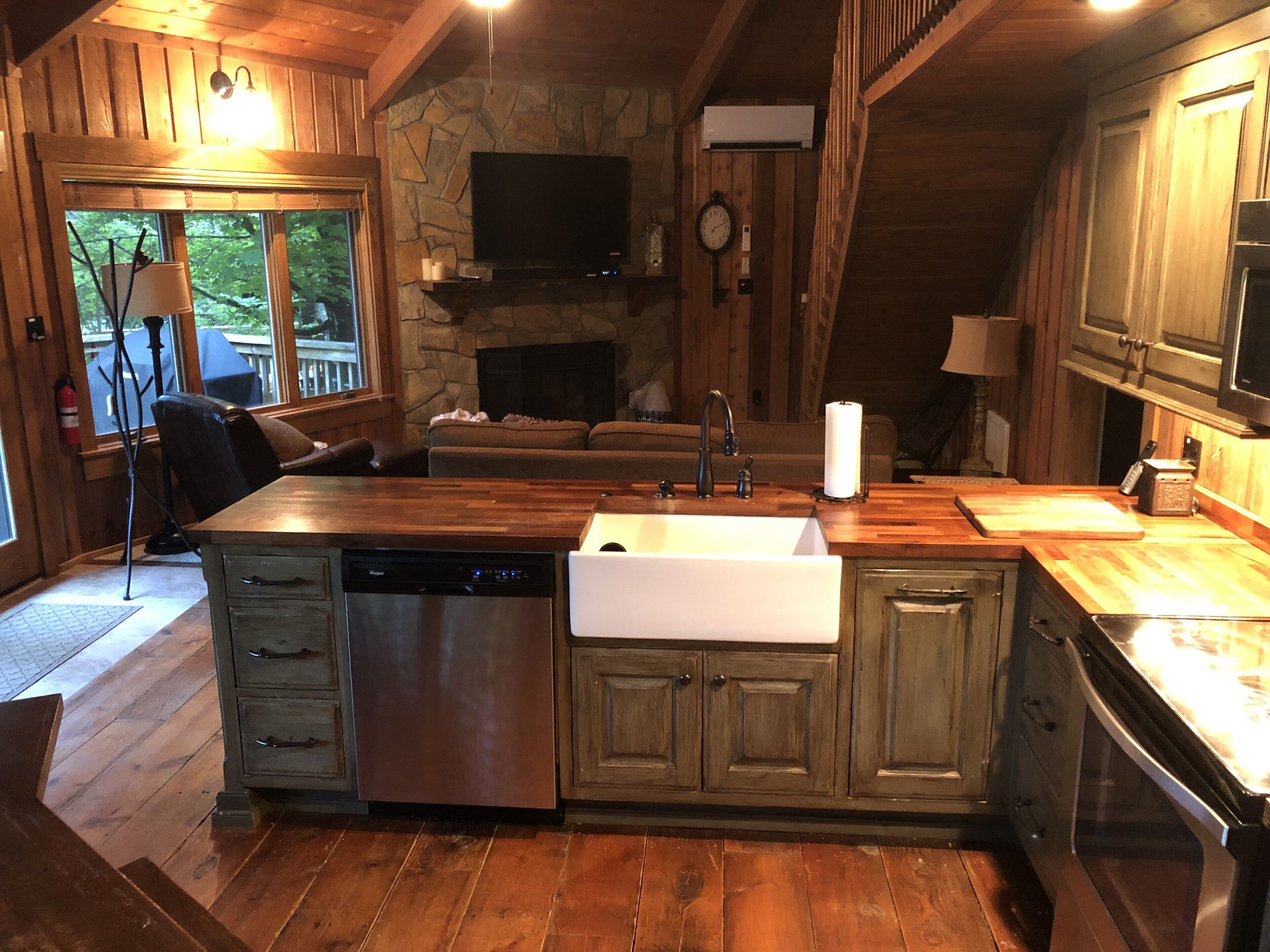 A rustic kitchen with a stone fireplace, wooden cabinets, and a large island with a sink.