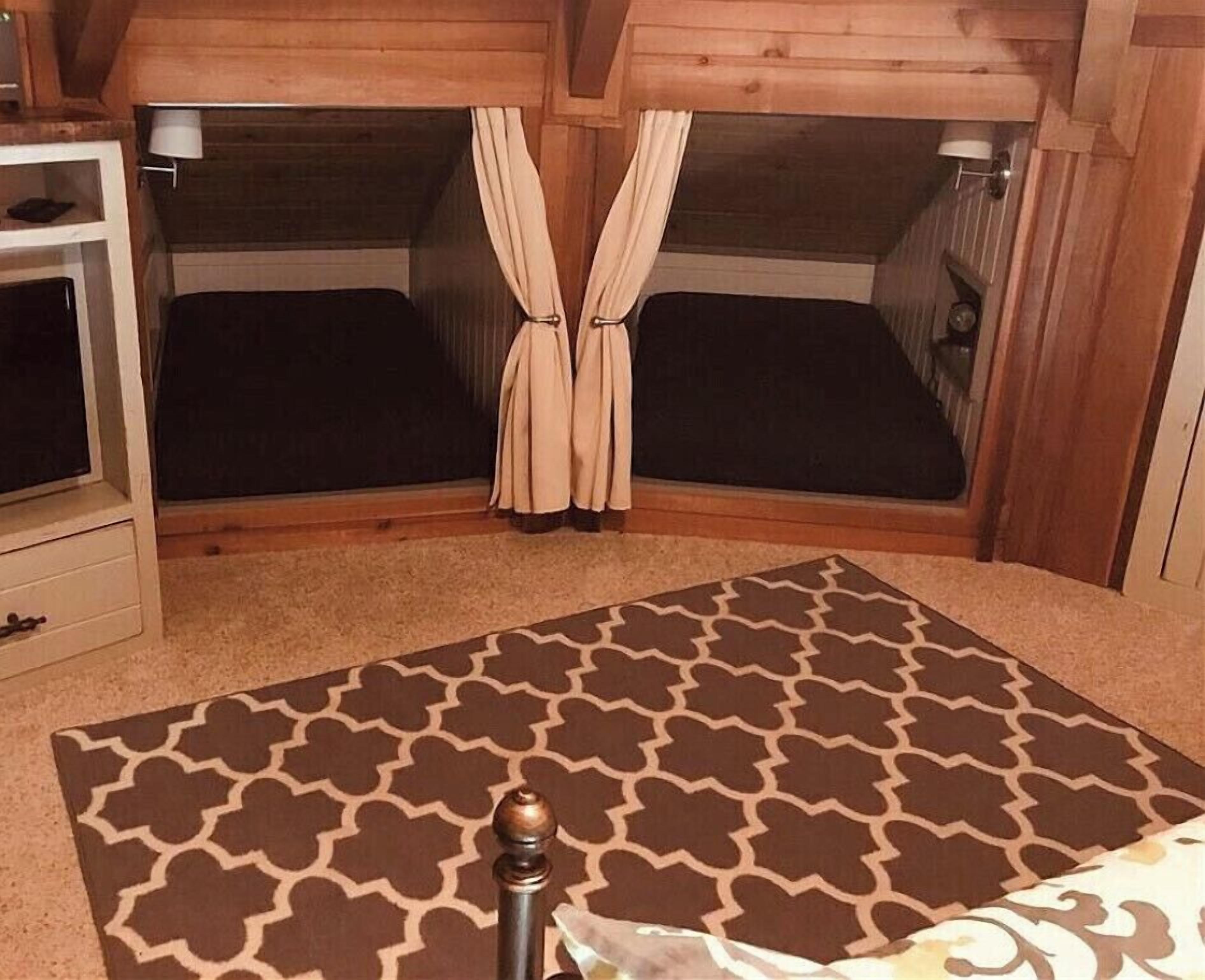 A room with two beds, a wooden ceiling, a small white cabinet, and a patterned rug.