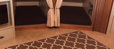 A room with two beds, a wooden ceiling, a small white cabinet, and a patterned rug.