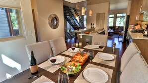 A dining area with a table set for four, including plates, wine glasses, and a casserole dish. A bottle of wine is on the table, and there is a staircase leading to another room. - Downtown Walla Walla Townhome · Walk to Main St · Rooftop + Garage (Walla Walla)