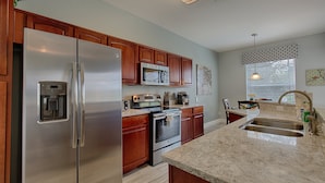 A modern kitchen with stainless steel appliances, wooden cabinets, and a granite countertop. - Welcome to The Windsor Fantasy with Brand New Professional Arcade Room! (Kissimmee)