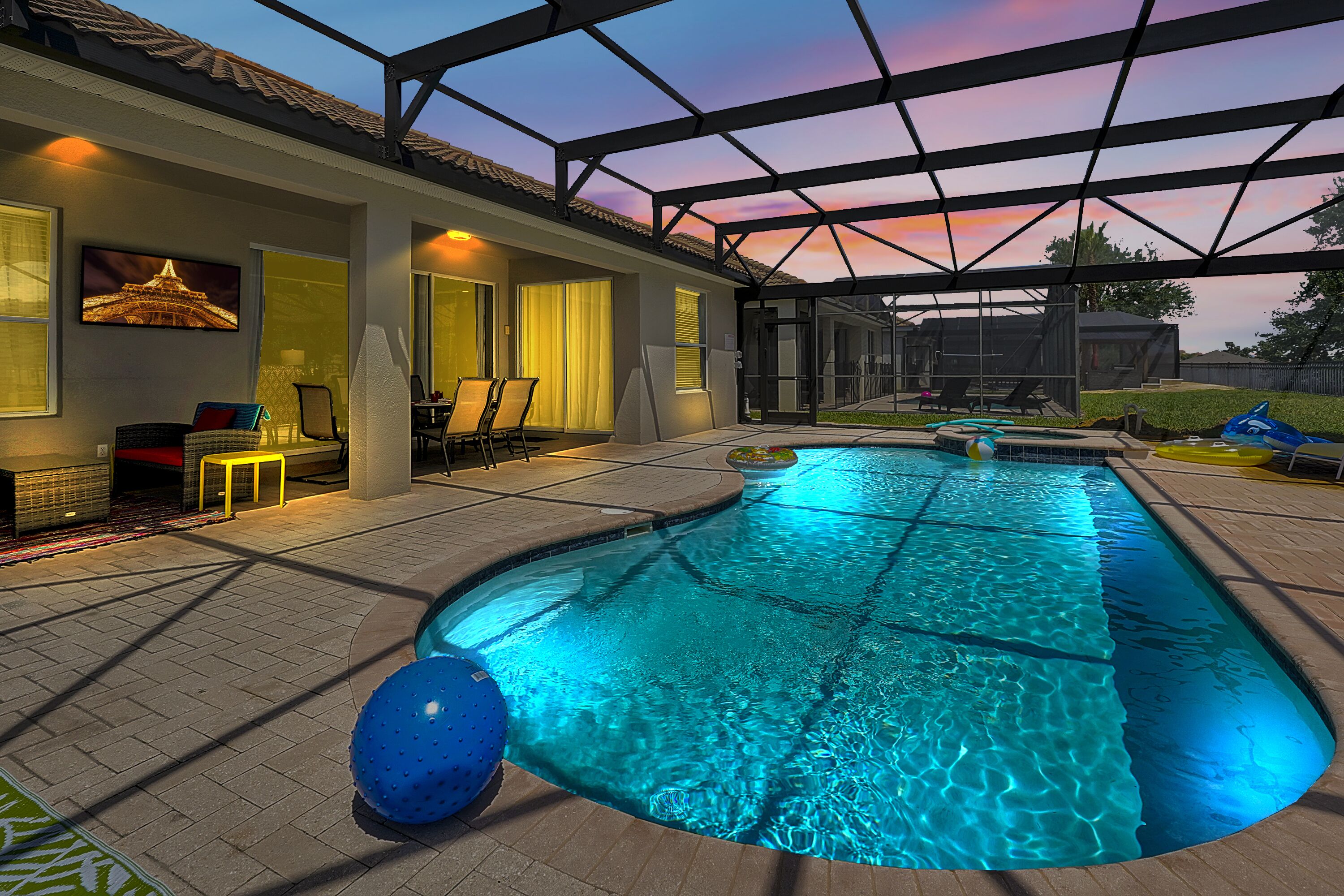 A swimming pool with a covered patio area, a seating area with chairs, and a view of the sunset.