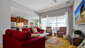 A spacious living room with a red sofa, patterned armchairs, and a yellow armchair. A large window provides a view of the outdoors.