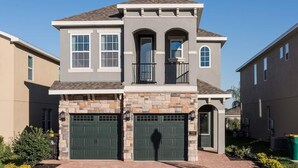 A two-story house with a stone facade, two green garage doors, and a small balcony. - Delightful Home with Entertainment Loft at Encore (Kissimmee)