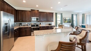A modern kitchen with dark wood cabinets, stainless steel appliances, and a granite countertop. - Delightful Home with Entertainment Loft at Encore (Kissimmee)