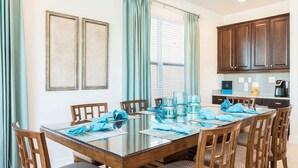 A dining area with a glass table, wooden chairs, teal curtains, and framed artwork on the wall. - Delightful Home with Entertainment Loft at Encore (Kissimmee)