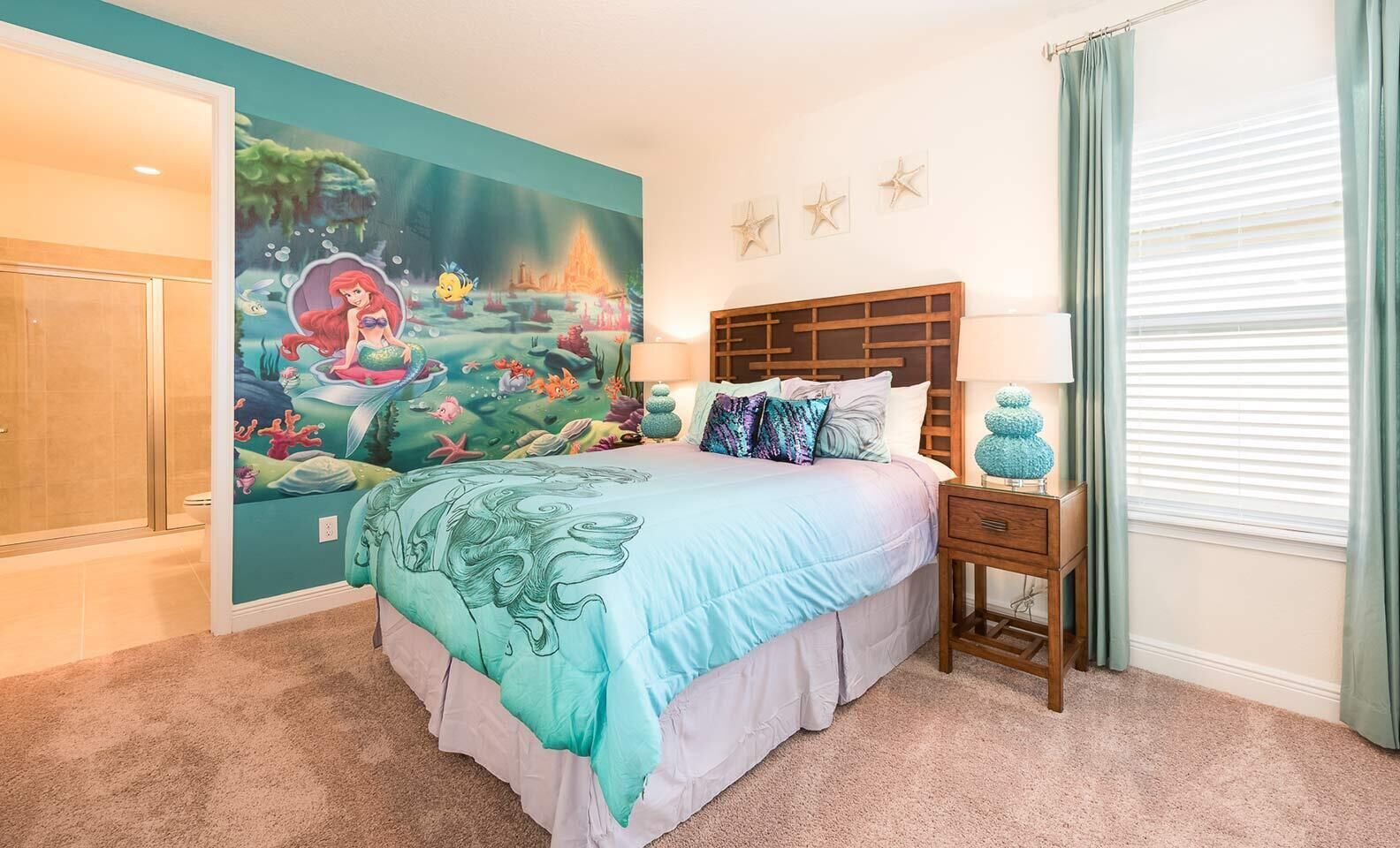 A bedroom with a large mural of an underwater scene, a bed with a blue and white bedspread, a wooden headboard, a nightstand with a lamp, and a window with curtains.