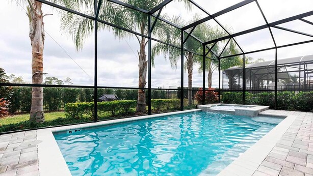Una piscina con recinto in vetro, circondata da palme e un giardino curato.