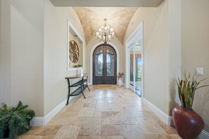Ein Flur mit einer Chandelieber, einer Tür mit Dekorationsglas und einer Kübelpflanze.