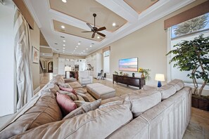 A spacious living room with a large sectional sofa, a ceiling fan, recessed lighting, and a television on a wooden console.