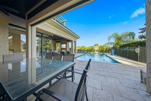 A glass-top table with chairs, a pool, and a covered patio area.